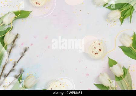 Weiße Tulpen und Katzenzweige in einem Rahmen angeordnet, cremefarbene Muffins auf einem Tisch flach liegen. Stockfoto