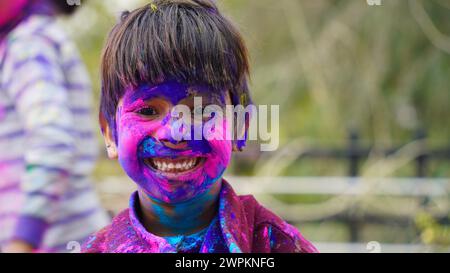 Glückliche indische Freunde oder Kinder, die das Hindufest von Holi feiern, indem sie sich gegenseitig Farben auftragen, beste Freunde. Weibliche Geschwister, die einen Teller halten Stockfoto