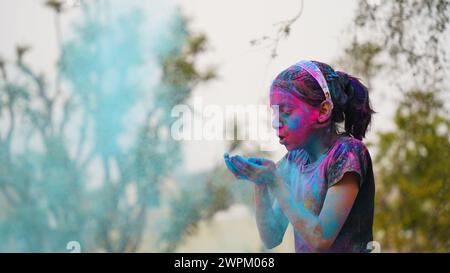 Glückliche indische Freunde oder Kinder, die das Hindufest von Holi feiern, indem sie sich gegenseitig Farben auftragen, beste Freunde. Weibliche Geschwister, die einen Teller halten Stockfoto