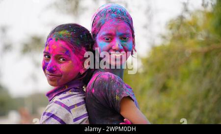 Glückliche indische Freunde oder Kinder, die das Hindufest von Holi feiern, indem sie sich gegenseitig Farben auftragen, beste Freunde. Weibliche Geschwister, die einen Teller halten Stockfoto