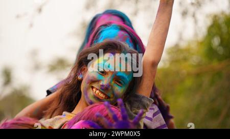 Junge süße, fröhliche kleine Mädchen Kind mit aufgetragenem holi Farben Pulver zeigt bunte Hände zur Kamera während der holi Festivalfeier Stockfoto