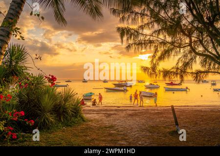 Blick auf Boote und Menschen am öffentlichen Strand Mon Choisy bei Sonnenuntergang, Mauritius, Indischer Ozean, Afrika Stockfoto