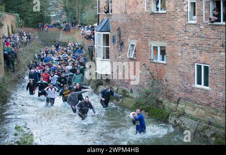 02/16 Spieler jagen den Ball durch Henmore Brook, während das Royal Shrovetide Football Match durch die Stadt Ashbourne in Derbyshire ausgetragen wird. U' Stockfoto