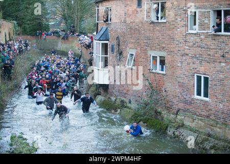 02/16 Spieler jagen den Ball durch Henmore Brook, während das Royal Shrovetide Football Match durch die Stadt Ashbourne in Derbyshire ausgetragen wird. U' Stockfoto