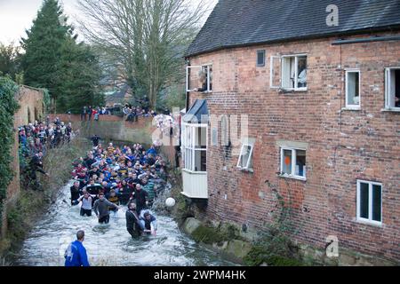 02/16 Spieler jagen den Ball durch Henmore Brook, während das Royal Shrovetide Football Match durch die Stadt Ashbourne in Derbyshire ausgetragen wird. U' Stockfoto