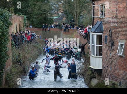 02/16 Spieler jagen den Ball durch Henmore Brook, während das Royal Shrovetide Football Match durch die Stadt Ashbourne in Derbyshire ausgetragen wird. U' Stockfoto