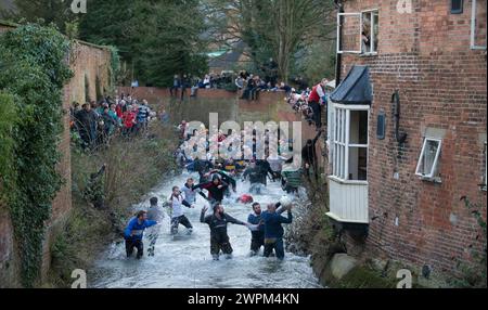 02/16 Spieler jagen den Ball durch Henmore Brook, während das Royal Shrovetide Football Match durch die Stadt Ashbourne in Derbyshire ausgetragen wird. U' Stockfoto