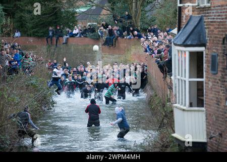 02/16 Spieler jagen den Ball durch Henmore Brook, während das Royal Shrovetide Football Match durch die Stadt Ashbourne in Derbyshire ausgetragen wird. U' Stockfoto