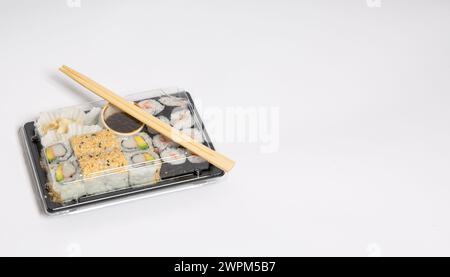 Sushi zum Mitnehmen in einer schwarzen Kiste mit Holzstäbchen auf weißem Hintergrund Stockfoto