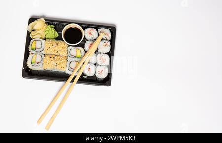 Sushi zum Mitnehmen in einer schwarzen Kiste mit Holzstäbchen auf weißem Hintergrund Stockfoto