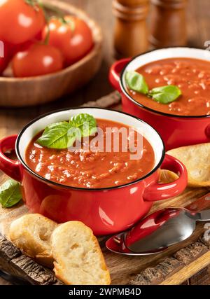 Schüssel Tomatensuppe garniert mit Basilikumblättern und gerösteten Baguetteschnitten auf Holztablett Stockfoto