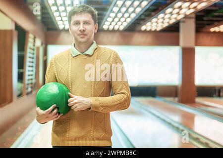 Lächelnder Mann, der grüne Bowlingball auf der Bowlingbahn hält. Stockfoto