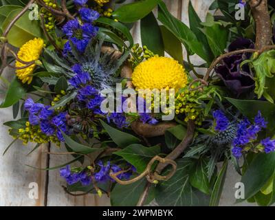 Nahaufnahme eines Frühjahrskranzes mit violetten und gelben Blumen und verdrehten Haselnusszweigen auf rustikalem, weiß getünchten Hintergrund aus Holz. Stockfoto