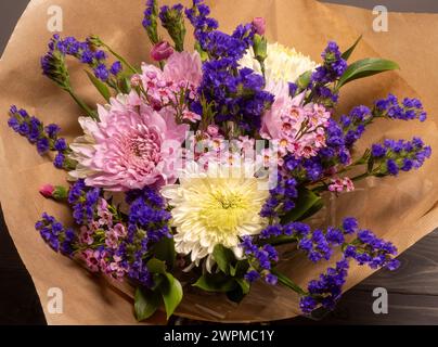 Blick aus der Vogelperspektive auf einen Blumenstrauß aus rosa und violetten Blumen, die in braunes Papier gewickelt sind. Stockfoto
