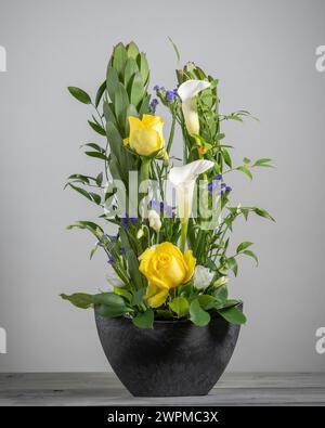 Blumenanordnung aus gelben Rosen, weißen Calla-Lilien, violettem statice und grünem Proteas auf grauem Hintergrund. Stockfoto