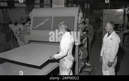 1950er Jahre, historisch, zwei männliche Arbeiter in Overalls in einer Produktionshalle der Camas Paper Mill, einer Senior, beaufsichtigte einen jüngeren Arbeitskollegen, als er Holzplatten in eine Maschine, eine Hyland 153, bei der Crown Zellerbach Corporation, WA, USA, einspeist. Das Geschäft geht auf das Jahr 1832 zurück und Anthony Zellerbach, jüdischer Abstammung, emigrierte 1846 von Bayern nach Amerika, wo er die Zellerbach Paper Co gründete, die 1928 mit der Crown Williamette Paper Company fusionierte. Stockfoto