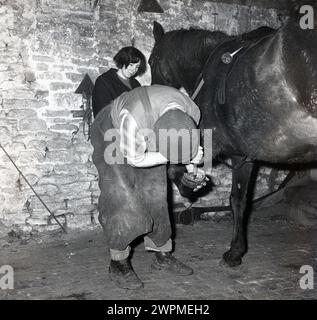 1970er Jahre, historisch, ein Farmer in einem Stall, der ein Pferd erschießt, Stallmädchen, das den Kopf des Tieres hält, England, Großbritannien. Stockfoto