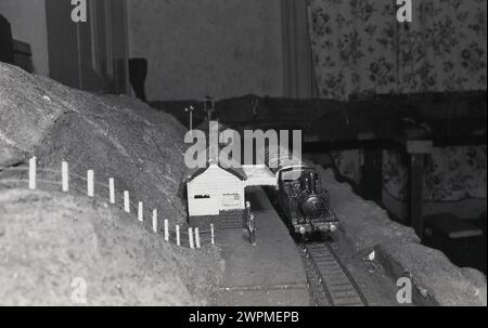 1950er Jahre, historisch, Innenraum eines Hauses, Modellbahn, Bild zeigt eine Modelldampfbahn auf einer Bahnstrecke an einem Bahnsteig. Stockfoto