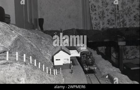 1950er Jahre, historisch, Innenraum eines Hauses, Modellbahn, Bild zeigt eine Modelldampfbahn auf einer Bahnstrecke an einem Bahnsteig. Stockfoto