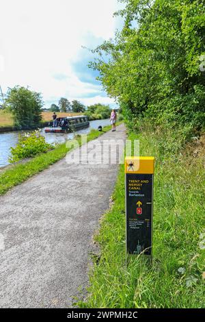 Ein Informationsschild oder ein Wegweiser auf dem Trent and Mersey Canal, mit einer Frau, die ihren Hund begleitet, Barlaston, Stoke on Trent, Staffordshire, England, UK Stockfoto