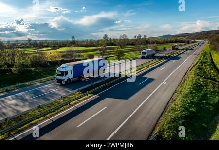 Straßenverkehr. Transportwagen in Schlangen, die auf einer Landstraße unter einem wunderschönen blauen Himmel vorbeifahren Stockfoto