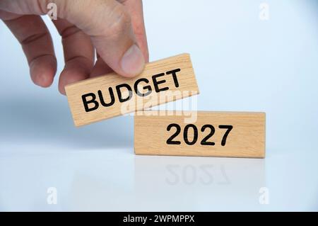 Hand haltender Holzblock mit Budget 2027 Text auf weißem Hintergrund. Konzept der jährlichen Budgetierung Stockfoto