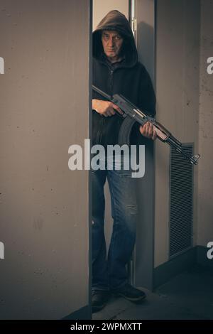 Mann in schwarzem Kapuzenhemd, bewaffnet mit automatischer Waffe, auf der Suche nach einer Gefahr Stockfoto