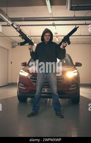 Mann in schwarzem Kapuzenhemd, bewaffnet mit automatischer Waffe, auf der Suche nach einer Gefahr Stockfoto