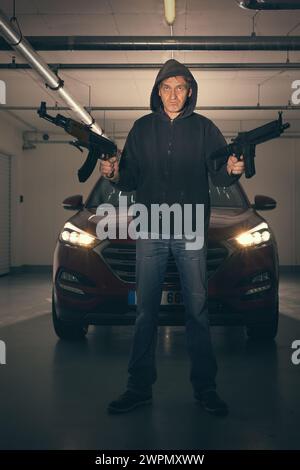 Mann in schwarzem Kapuzenhemd, bewaffnet mit automatischer Waffe, auf der Suche nach einer Gefahr Stockfoto