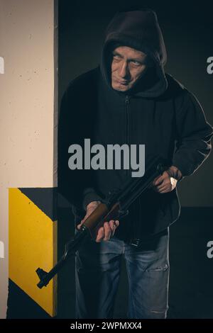 Mann in schwarzem Kapuzenhemd, bewaffnet mit automatischer Waffe, auf der Suche nach einer Gefahr Stockfoto