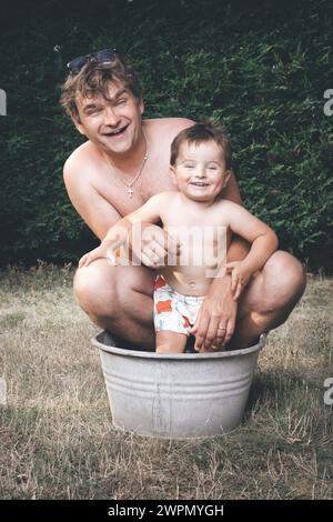 Vater und Sohn chillen in einer kleinen Retro-Blechbadewanne Stockfoto