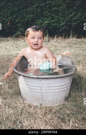 Kleiner Junge chillt in einer kleinen Retro-Blechbadewanne Stockfoto