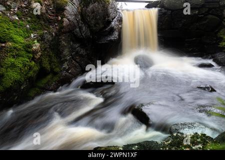 Ein kleiner Mann hat Wasserfall und Strömung mit Felsen auf einem Langzeitfoto gemacht. Stockfoto