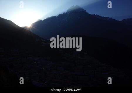 Erster Blick auf die Morgensonne hinter dem Berg Thamserku, das Dorf Namche Bazaar im Schatten, den Nationalpark Sagarmatha, das Khumbu-Tal, den Himalaya, Nepal Stockfoto