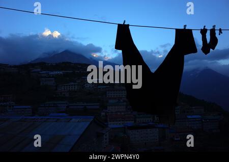 Hosen und Socken trocknen am Wäscheseil mit abendlichem Blick auf das Dorf Namche Bazaar und letzte Sonne auf dem Berg Thamserku, Sagarmatha Nationalpark, Stockfoto