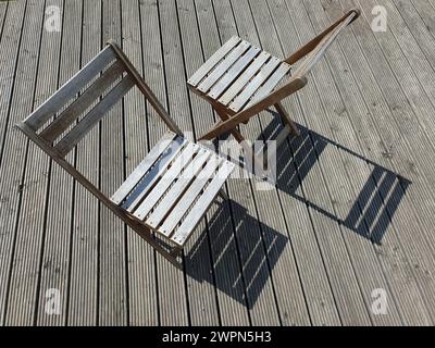 Zwei Holzstühle stehen sich im Sonnenlicht auf einer Holzterrasse gegenüber Stockfoto