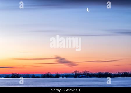 Sonnenaufgang mit Halbmond über dem Heisterbusch bei Flut auf der Elbe bei Bleckede Stockfoto