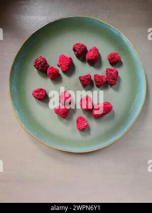 Eine grüne Platte mit 15 getrockneten roten Himbeeren auf grauem Hintergrund Stockfoto