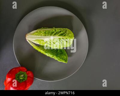 Salatherz, kleiner Römersalat, ganze grüne Salatblätter auf einem Teller mit rotem Glockenpfeffer am Rand des Tellers Stockfoto