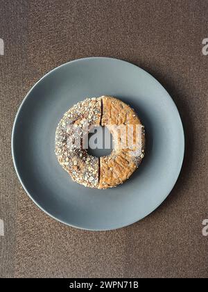 Ein Bagel wird in zwei Hälften geschnitten, wobei die Unterseite und die Oberseite mit Samen auf einer grauen Platte liegen Stockfoto