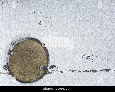 Spuren und Muster im Schnee und die schneebedeckte Mannlochabdeckung schaffen ein abstraktes Winterbild Stockfoto