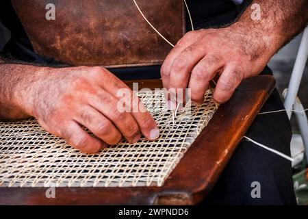 Die geschickten Hände eines Handwerkers beim Reparieren des Strohs eines Stuhls Stockfoto