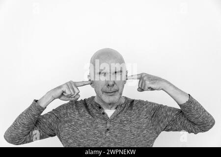 Reifer Mann mit den Fingern in den Ohren und geschlossenen Augen. Schwarz-weiß. Stockfoto