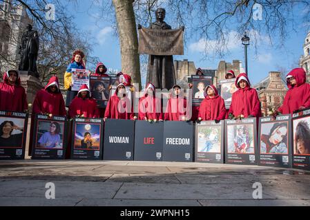 London, Großbritannien. März 2024. Iranische Frauen halten Plakate vor der Statue von Millicent Fawcett und verkleidet als Magd Charaktere aus dem Buch Handmaid's Tale, das von der Margaret Atwood geschrieben wurde. Iranische Frauen versammelten sich auf dem Parlamentsplatz bei der Statue von Millicent Fawcett, um den Internationalen Frauentag und ihren Kampf gegen das iranische Regime zu feiern. Quelle: SOPA Images Limited/Alamy Live News Stockfoto