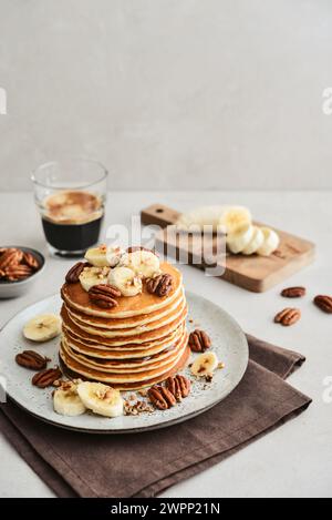 Teller mit Ahorn-Pekannkuchen mit frischen Bananen und Kaffee im Hintergrund. Stockfoto