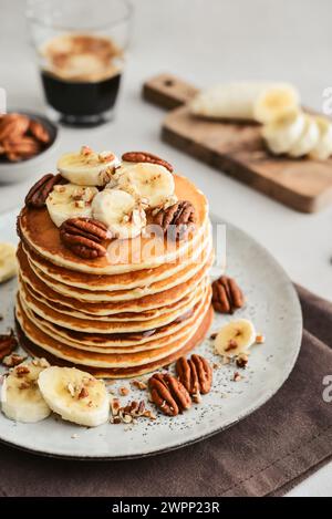 Teller mit Ahorn-Pekannkuchen mit frischen Bananen und Kaffee im Hintergrund. Stockfoto