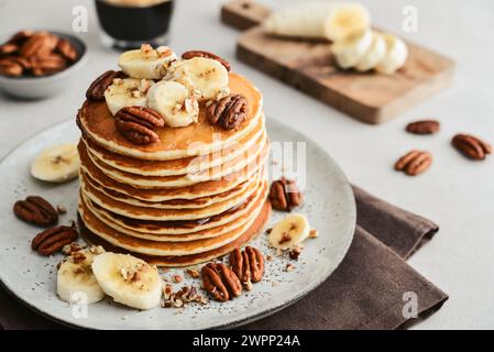 Teller mit Ahorn-Pekannkuchen mit frischen Bananen und Kaffee im Hintergrund. Stockfoto