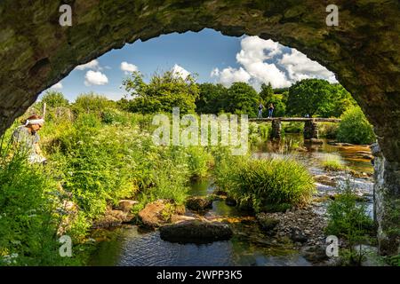 Touristen auf der mittelalterlichen Steinplattenbrücke Clapper Bridge in Postbridge, Dartmoor, Devon, England, Großbritannien, Europa Stockfoto