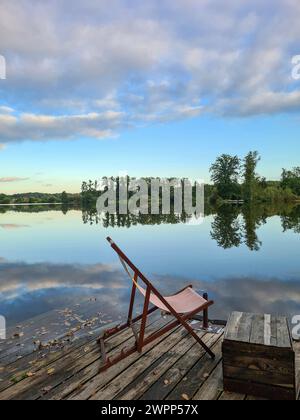 Ein Liegestuhl steht auf einer Holzplattform am Seeufer, Blick auf Wasser und Himmel mit Wolken, Wannsee, Berlin, Deutschland Stockfoto