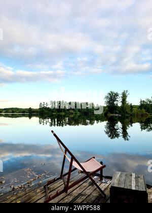 Ein Liegestuhl steht auf einer Holzplattform am Seeufer, Blick auf Wasser und Himmel mit Wolken, Wannsee, Berlin, Deutschland Stockfoto